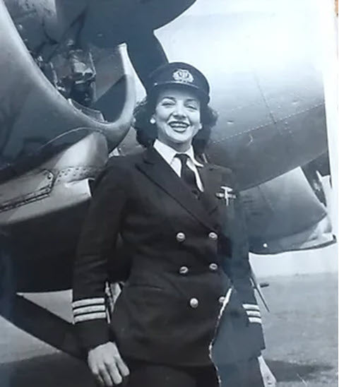 Jackie Moddridge, aka The Spitfire Girl, in front of a multi-engine aircraft in her pilot's uniform.