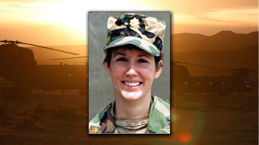 A photograph of U.S. Army Major Marie T. Rossi-Clayton with CH-47 Chnook helicopters behind her in the desert.