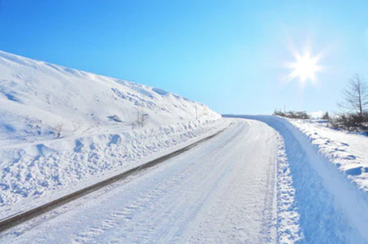 A road through snow on a bright winter day showing how bright the sunlight can be under these conditions.