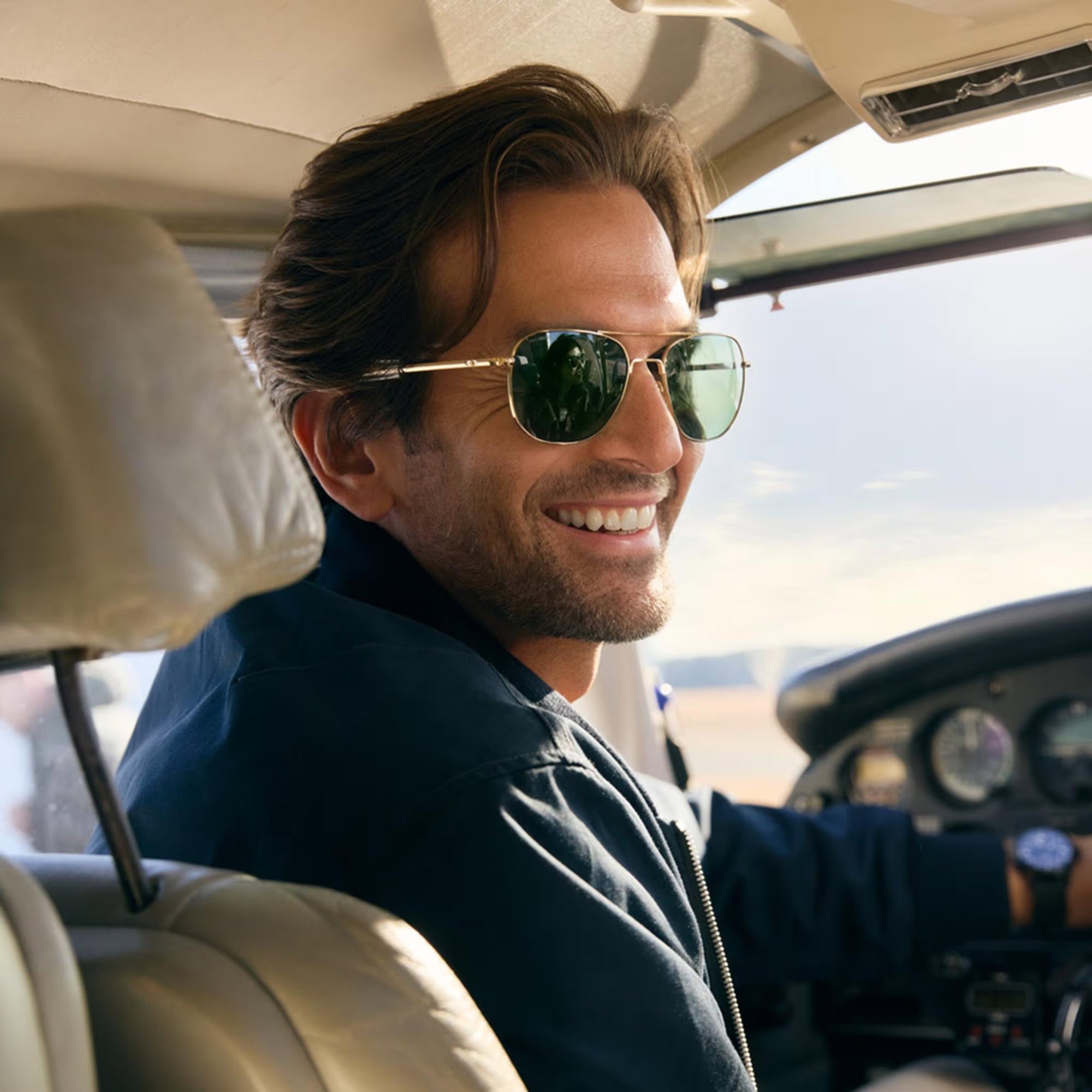 Man wearing a pair of AO Eyewear Original Pilot aviator sunglasses inside an airplane cockpit with a blurred outdoor background